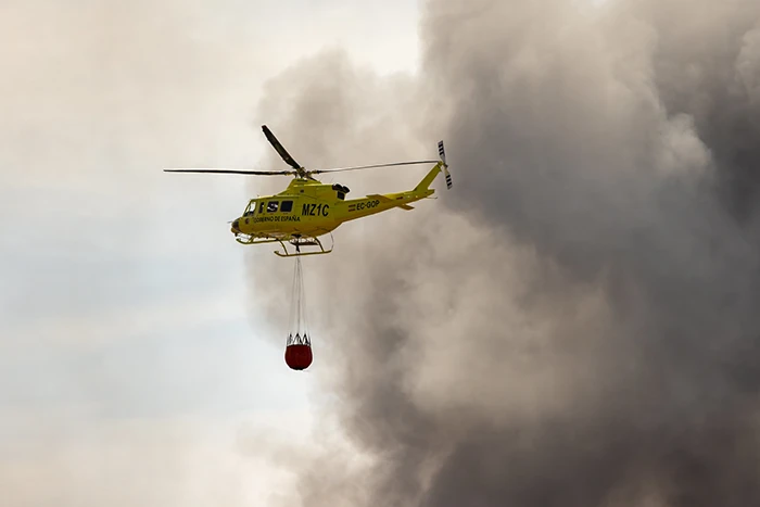 Helicóptero del operativo contra incendios descargando agua sobre un gran foco de fuego y humo.