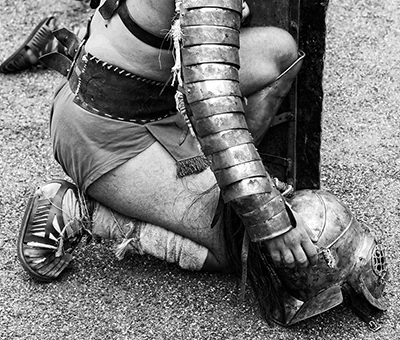 Gladiador romano recreado, arrodillado con armadura y casco en la mano durante una representación histórica. Emerita Lvdica. Mérida.