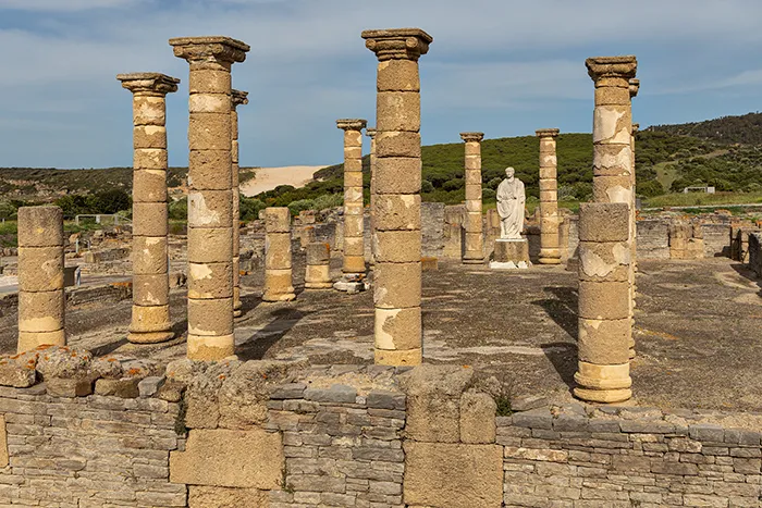 Columnas de la basílica de Baelo Claudia con la estatua de Trajano y la duna de Bolonia al fondo.
