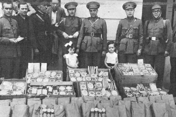 Efectivos del Cuerpo de Carabineros posan junto a mercancía incautada durante la Guerra Civil Española, acompañados de civiles y niños.