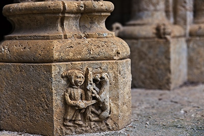 Figura humana enfrentada a una criatura en una escena simbólica del claustro románico.