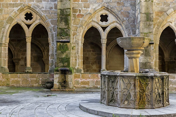 Fuente gótica del claustro de la Catedral de Plasencia, con decoración vegetal y heráldica, frente a los arcos apuntados de estilo cisterciense.