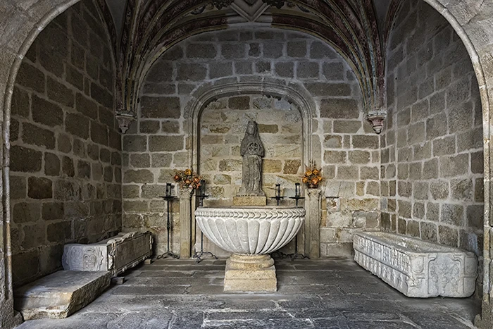 Pila bautismal románica con decoración acanalada en capilla del claustro de la Catedral de Plasencia, acompañada de sepulcros y una escultura.