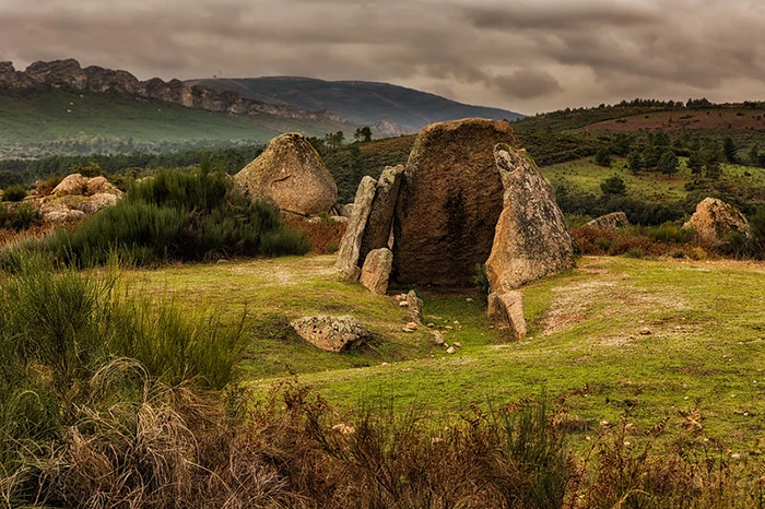 Dolmen Data I en La Aceña de la Borrega (Valencia de Alcántara, Cáceres): cámara megalítica de cinco ortostatos abierta al paisaje de dehesa, con sierras y cielo nuboso al fondo.