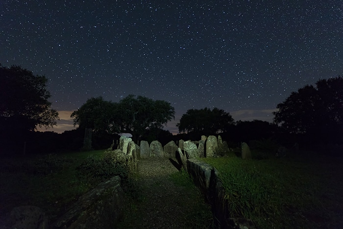 Acceso principal del Dolmen de la Gran Encina iluminado bajo un cielo estrellado, flanqueado por grandes piedras verticales.
