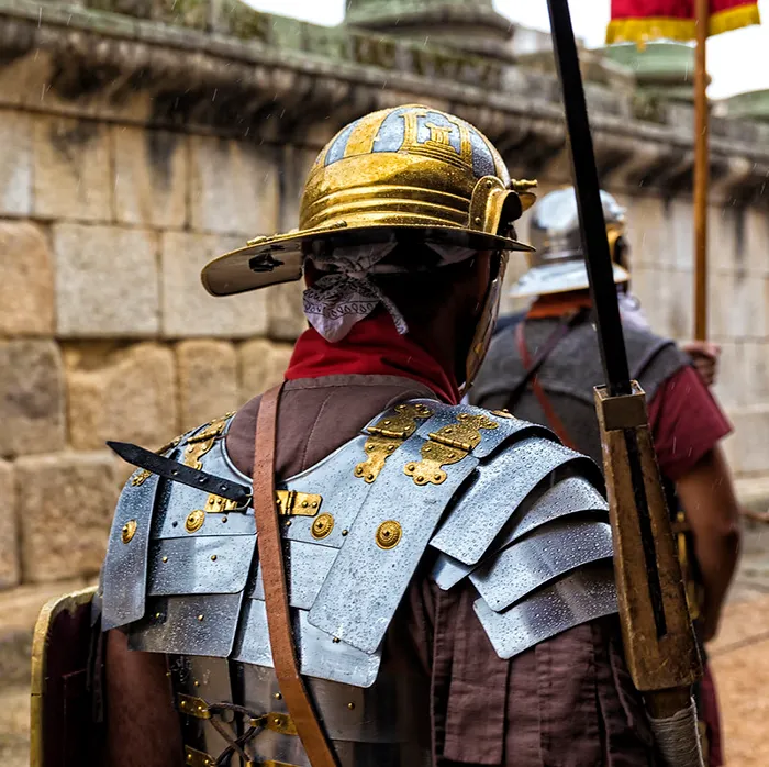 Recreación histórica de un legionario romano en Emerita Lvdica, con armadura metálica y casco dorado, marchando bajo la lluvia.