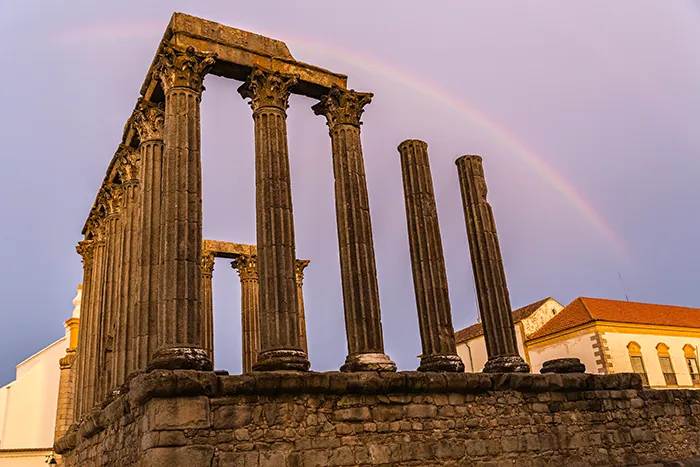 Templo romano de Évora iluminado por el atardecer con arco iris de fondo.