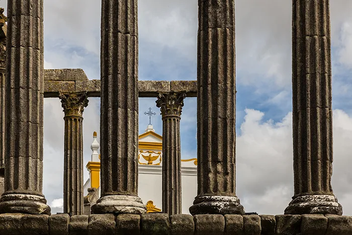 Columnas corintias del templo romano de Évora en primer plano con iglesia al fondo.
