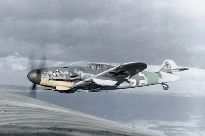 Caza alemán Messerschmitt Bf 109 en vuelo durante la Segunda Guerra Mundial, con camuflaje, nariz amarilla y emblemas de la Luftwaffe.