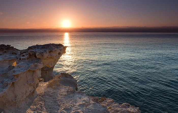 Formación rocosa blanca iluminada por el sol naciente reflejado en el Mediterráneo en calma.