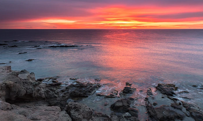 Costas erosionadas bajo un cielo púrpura, con reflejos anaranjados en el agua