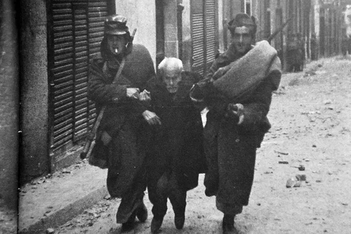 Una persona mayor es ayudada por dos combatientes en una calle de Teruel durante la batalla de la ciudad.