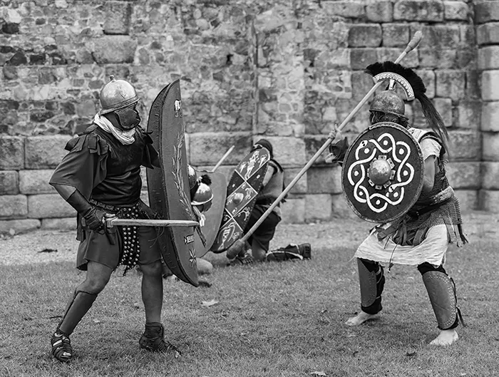 Recreación en Mérida de legionarios romanos combatiendo con escudos y espadas frente a murallas romanas.
