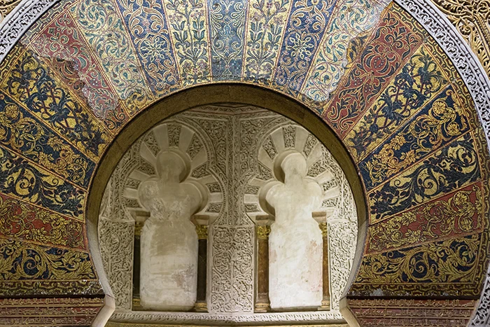 Vista frontal del mihrab de la Mezquita Catedral de Córdoba con mosaicos dorados y arcos ciegos trilobulados en piedra tallada.