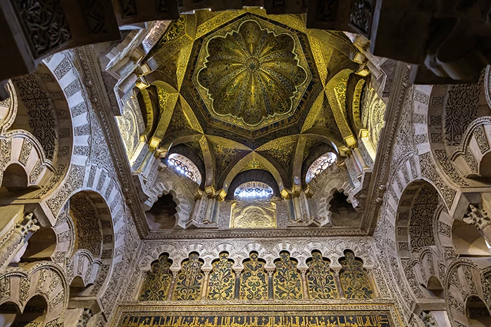 Cúpula dorada de la maqsura frente al mihrab de la Mezquita Catedral de Córdoba con nervaduras entrecruzadas y caligrafía cúfica.