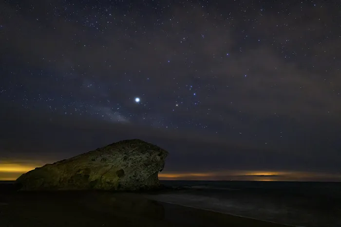Noche en la playa de Mónsul con cielo estrellado y roca volcánica.