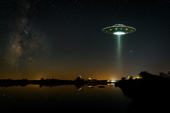 Simulación artística de un OVNI sobre el agua en Los Barruecos, bajo un cielo estrellado.
