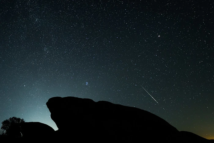 Cielo estrellado con una estrella fugaz atravesando el horizonte sobre las formaciones rocosas de Los Barruecos.