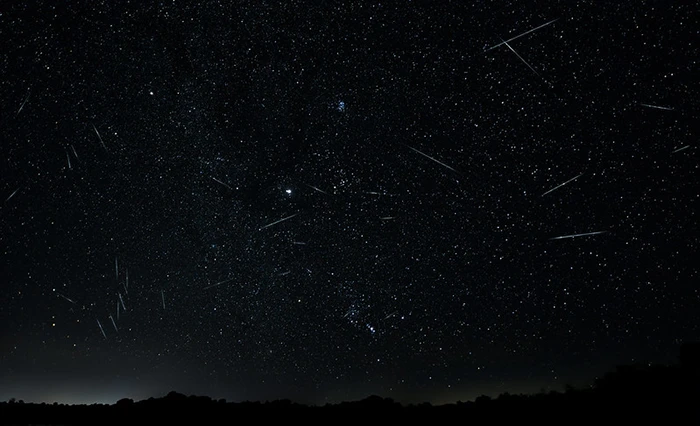 Cielo nocturno con múltiples meteoros de las Perseidas sobre el horizonte oscuro.