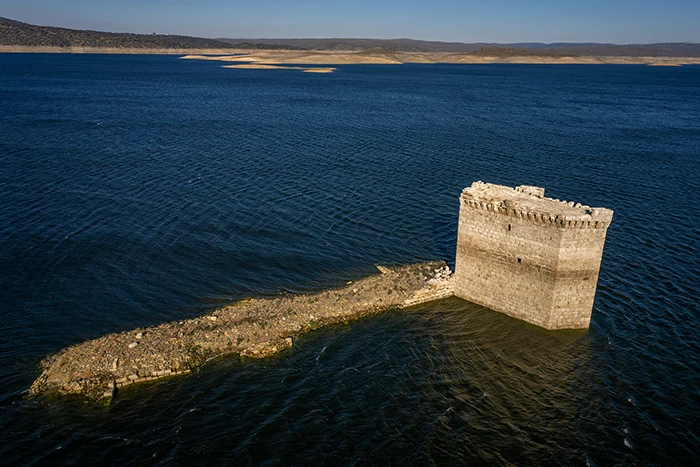 La Torre de Floripes parcialmente sumergida en el embalse de Alcántara, rodeada por aguas azules en calma